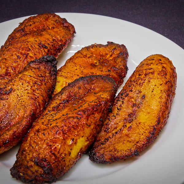 Four golden-brown fried maduros, or sweet plantains, on a white plate at Rumba Cuban Cafe.