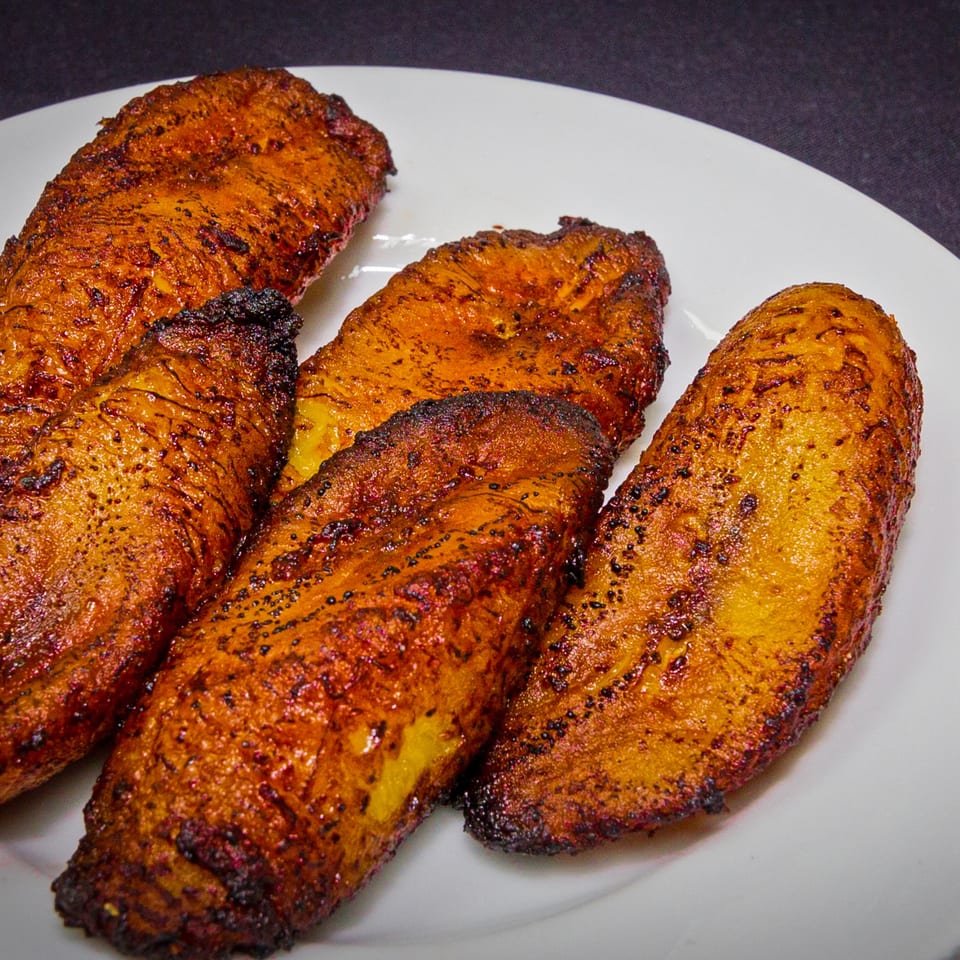 Four golden-brown fried maduros, or sweet plantains, on a white plate at Rumba Cuban Cafe.