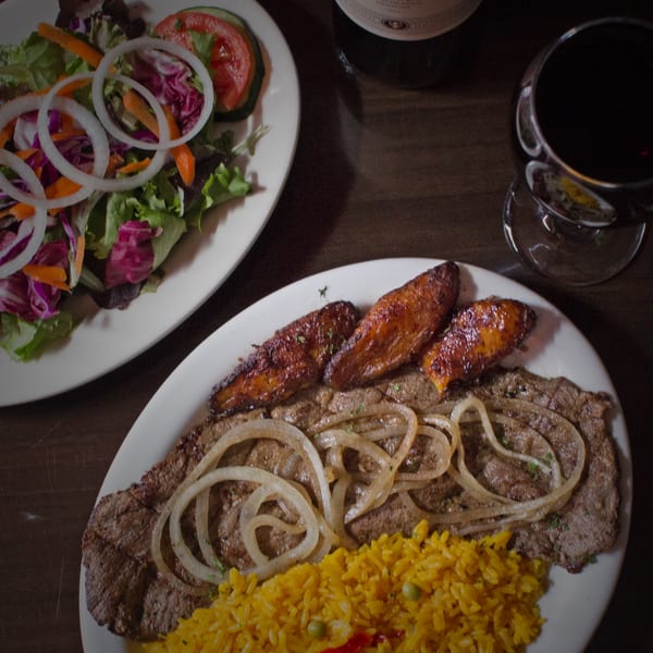 Cuban steak with onions, yellow rice, fried plantains, and a side salad with red wine.