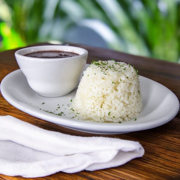 A white bowl of black beans and a mound of white rice with parsley on a white plate.