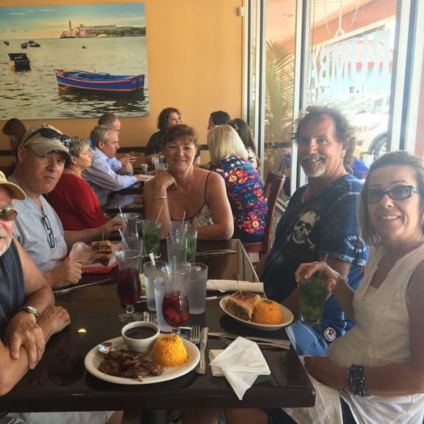 Patrons enjoying Cuban food and drinks at Rumba Cuban Cafe, with a large Havana-themed mural in the background.