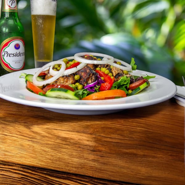 Cuban grilled chicken salad with onions, peas, and peppers, next to a President beer.