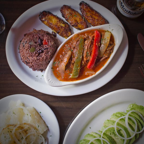 Rumba Cuban Cafe's Ropa Vieja with rice, plantains, yucca, and avocado salad on a wooden table.