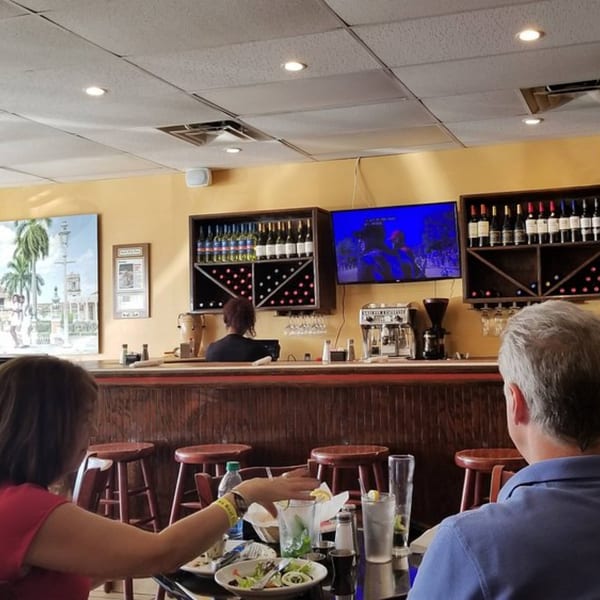 Diners seated at tables and a bar with a TV, wine rack, and coffee machine at Rumba Cuban Cafe.