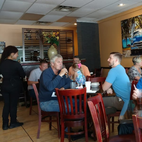 A server attends to guests dining at tables in the Rumba Cuban Cafe, with a vintage car mural in the background.
