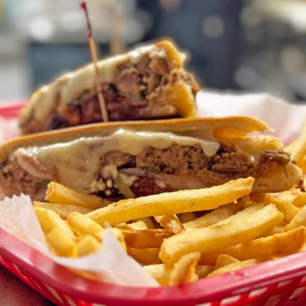 Two Cuban sandwiches with melted cheese and fries in a red basket at Rumba Cuban Cafe.