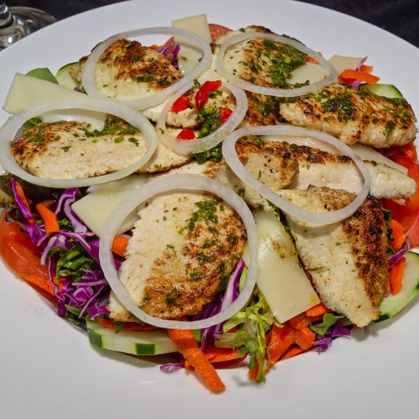 Grilled chicken breast slices with onions, red peppers, and fresh herbs on a colorful salad.