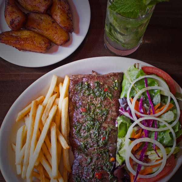 Cuban skirt steak with chimichurri, fries, salad, fried plantains, and a mojito.