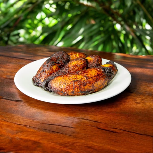 A white plate holds several dark, caramelized Cuban maduros (sweet plantains) on a wooden table.