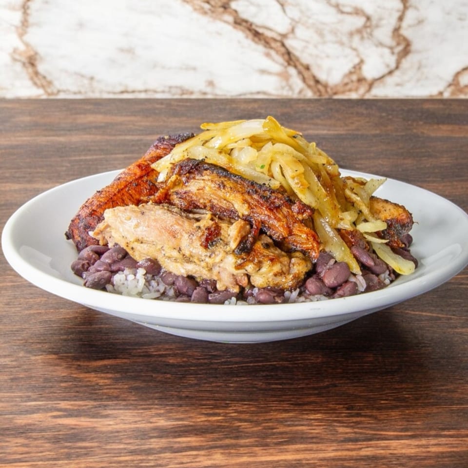 Grilled chicken topped with sautéed onions and peppers, served over rice and beans on a white plate.