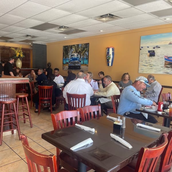 Diners enjoying meals at tables and a bar in a brightly lit Rumba Cuban Cafe dining room.