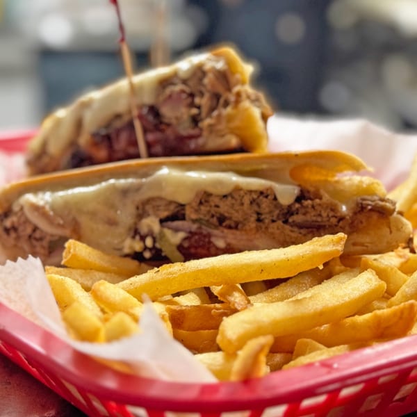 A Cuban sandwich with melted cheese and fries in a red basket at Rumba Cuban Cafe.